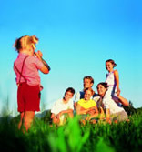 Girl takes a picture from the family sitting in the grass   