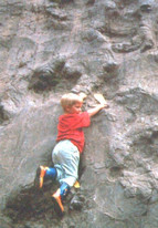 Young boy climbing a rock wall with dinosaur footprints