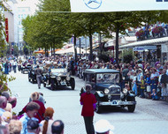 Four black, classic Daimler-Benz cars at a parade with a number of onlookers