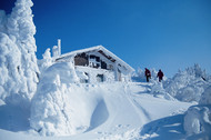 Two walkers in deep snow in front of a mountain hut